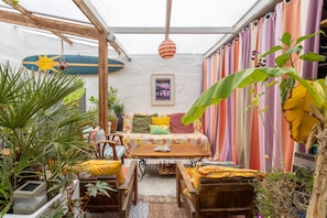 A cozy patio area with a wooden table, chairs, and a colorful striped curtain backdrop. - Sea, Countryside in the City Center – Rooms 1+2 (Douarnenez)