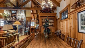 Une table de salle à manger en bois, des chaises, un sapin de Noël et une cheminée en pierre.