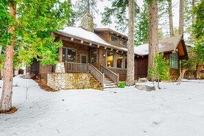 A cabin with a stone foundation, wooden exterior, and a porch with steps leading to a door.