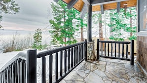 Un porche dallé de pierres, avec une balustrade noire, des poutres en bois et une vue sur des arbres verdoyants.