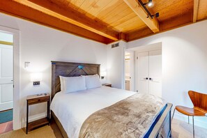 Ein Schlafzimmer mit Holzboden, einem Bett mit weißem Kopfteil, einem Nachttisch mit Lampe und einem Sessel.