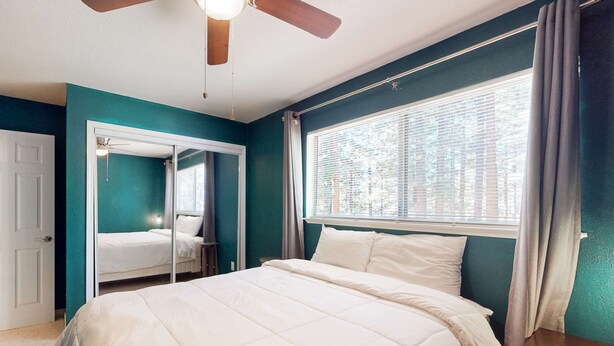 Un dormitorio con cama, ventilador de techo, ventana con cortinas y puerta.
