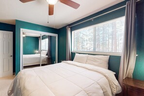 Ein Schlafzimmer mit einem Bett, einem Deckenventilator, einem Fenster mit Vorhängen und einer Tür.