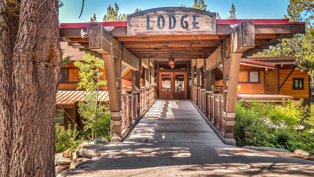 A lodge entrance with a wooden archway, a pathway leading to the building, and surrounding greenery. - Cozy studio condo with kitchenette, deck, WiFi, & nearby activities (Truckee)