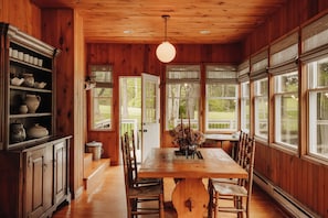 Un interior de madera con una mesa de comedor, sillas, una araña y ventanas amplias.