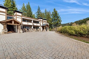 A multi-story building with a stone facade, large windows, and a paved driveway. - Cozy Condo with Wood Fireplace, Mountain Views- Walk to Lifts (Olympic Valley)