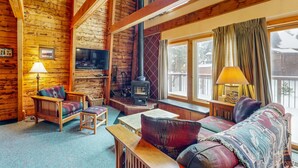 L’intérieur d’une cabane en rondins, avec une cheminée, des meubles en bois et de grandes fenêtres.