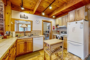 Cocina tipo cabaña de madera con encimera de madera, un lavamanos, lavavajillas, una mesa de madera y un refrigerador.