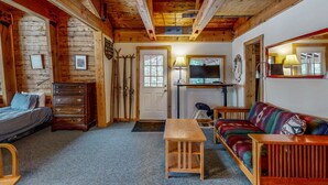 L’intérieur d’un chalet accueillant, avec un lit, une commode en bois, un canapé et un téléviseur.