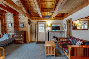 Interior acogedor de una cabaña con cama, cómoda de madera, sofá y televisor.