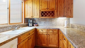 Una cocina con armarios de madera, encimera de granito, vinatero y una ventana.