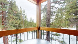 Un balcón de madera con barandilla de metal, con vistas a un paisaje nevado con pinos.