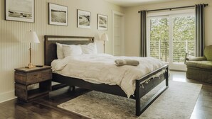 Un dormitorio con cama, mesitas de noche, cortinas en la ventana y cuadros en la pared.
