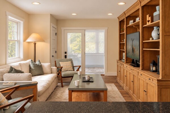A living room with a sofa, armchair, coffee table, and wooden cabinet with shelves.