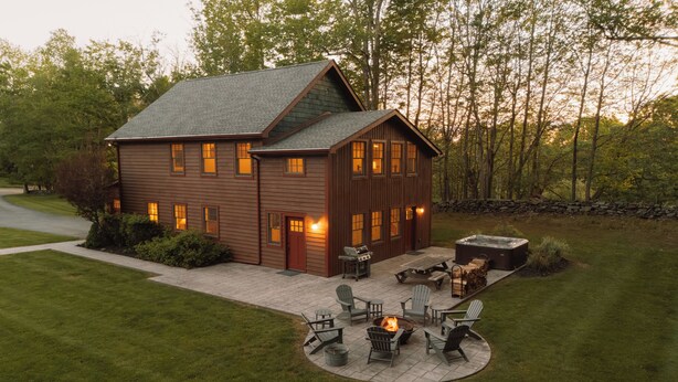 Casa de madera de dos pisos con un patio que tiene mobiliario exterior y una chimenea.