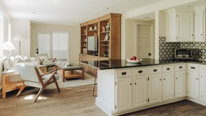Una cocina moderna con armarios blancos, una isla de madera y un comedor con sofá y sillas.
