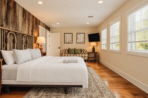A bedroom with a bed, a wooden headboard, a television, and a window with blinds.
