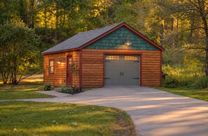 A wooden shed with a garage door, a small porch, and a pathway leading to it.