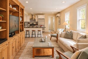 A spacious living area with a wooden entertainment unit, a sofa, a coffee table, and a kitchen in the background.