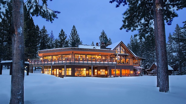 A large, multi-story lodge with a covered porch and multiple windows, surrounded by snow and trees. - Woodland Retreat with Private Multi-Level Deck & Backyard Creek (Truckee)