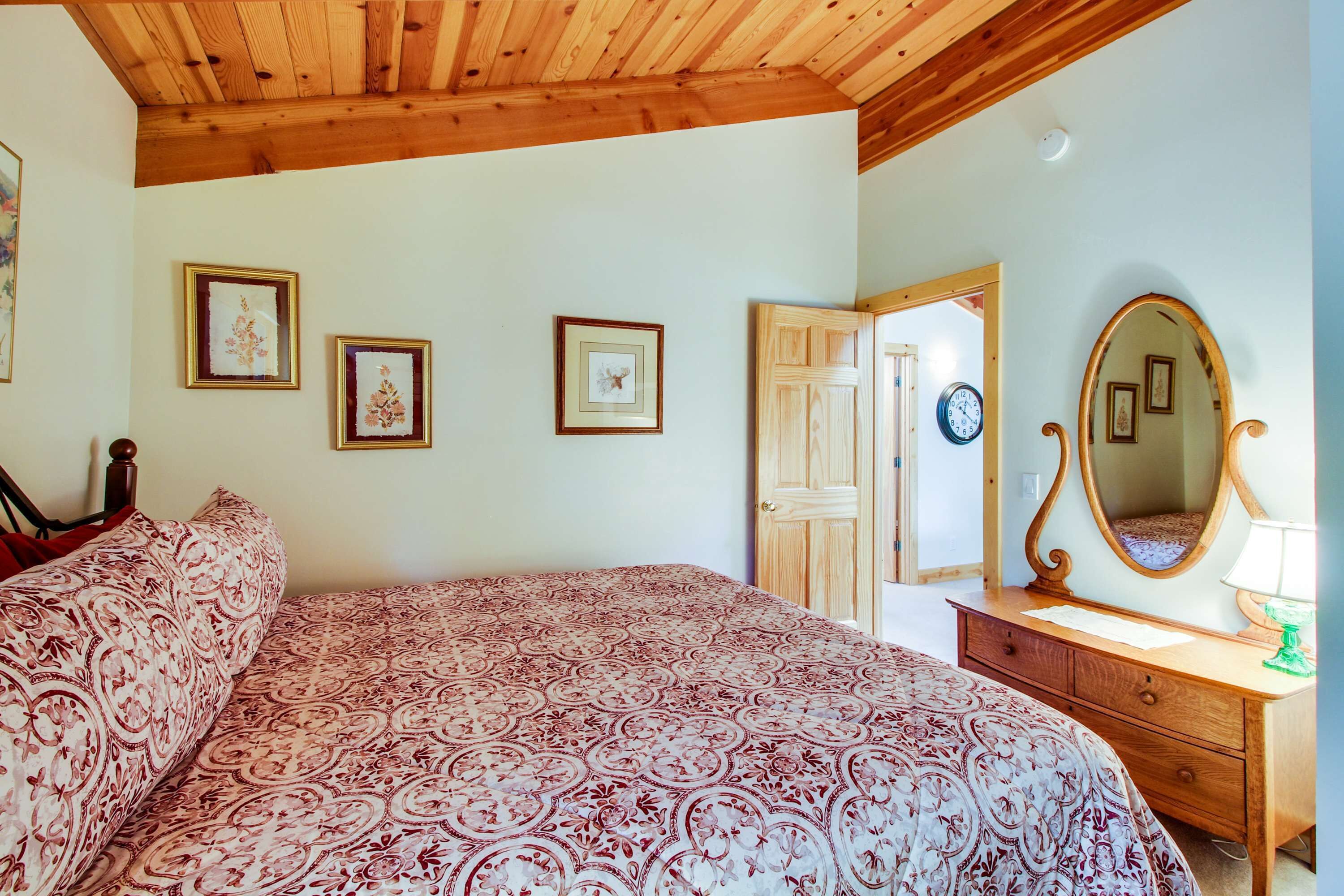 Une chambre à coucher avec un lit, une commode, un miroir et des tableaux encadrés accrochés au mur.
