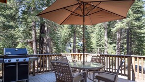 Eine Terrasse mit Grill, Tisch und Stühlen, umgeben von einem Holgitter und Bäumen.