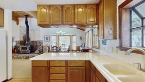 A kitchen with wooden cabinets, a large island, a stone fireplace, and a view of the dining area. - Rustic home with wood stove, deck, open floor plan, & nearby activities (Carnelian Bay)