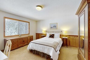 A bedroom with a large bed, wooden headboard, bedside tables with lamps, a window with blinds, a dresser, and a mirror. - Rustic home with wood stove, deck, open floor plan, & nearby activities (Carnelian Bay)