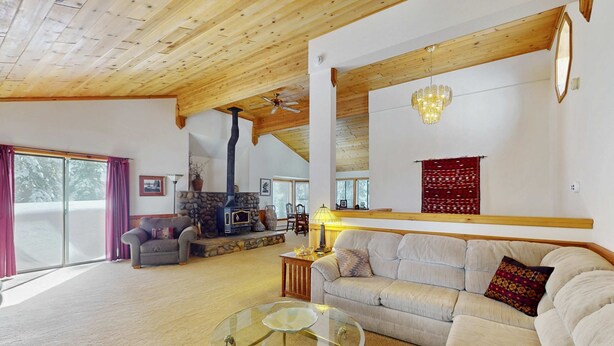 A spacious living room with a glass coffee table, a sofa, a fireplace, and a chandelier. - Rustic home with wood stove, deck, open floor plan, & nearby activities (Carnelian Bay)