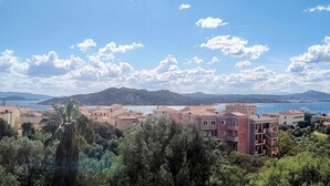 A coastal town with buildings, trees, and a mountain in the background. - Maison Angelo - Sea & mountain views, panoramic terrace in Sardinia (La Maddalena)