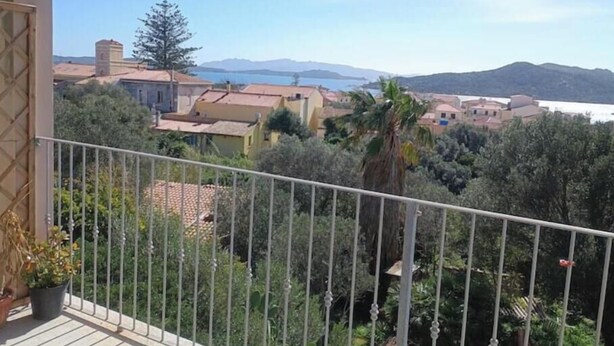 A balcony with a metal railing overlooking a coastal town with buildings and trees. - Maison Angelo - Sea & mountain views, panoramic terrace in Sardinia (La Maddalena)