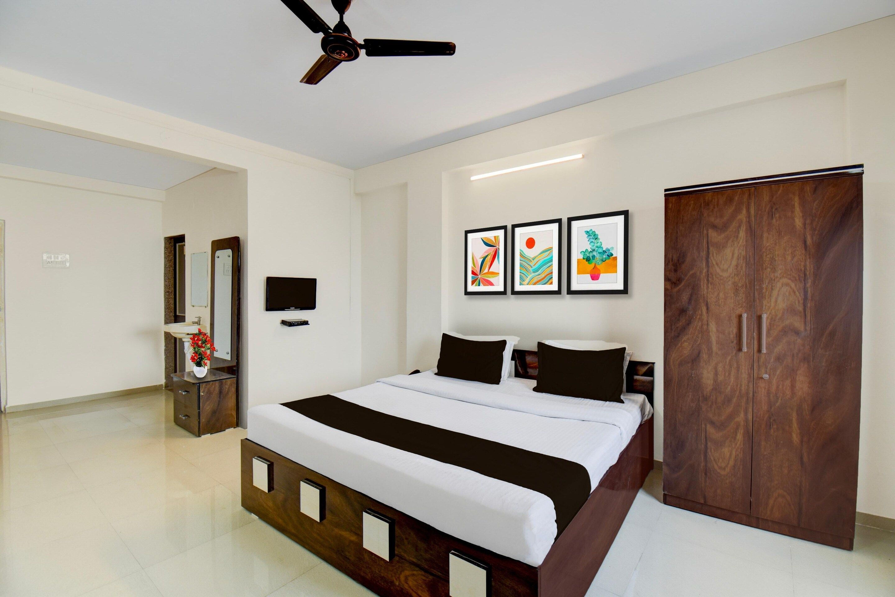 A bedroom with a bed, a wardrobe, a TV, and artwork on the wall.