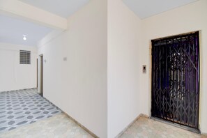 A hallway with a tiled floor, a door with a metal gate, and a vent on the wall. - Classic With Balcony Hotel Galaxy Inn (Junnar)