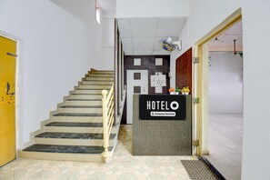 A hotel reception area with a staircase leading to a second floor, a reception desk, and a wall with a bulletin board. - Classic With Balcony Hotel Galaxy Inn (Junnar)