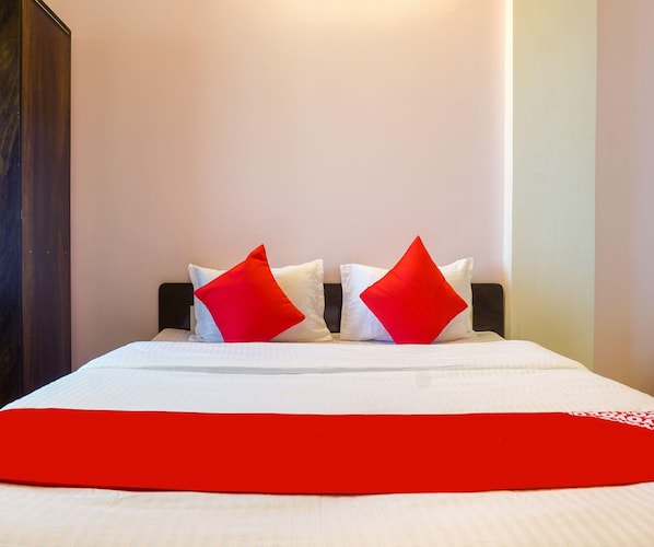 A bed with white bedding and two red pillows, a dark headboard, and a red accent on the bedspread.