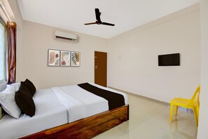 A hotel room with a bed, a ceiling fan, an air conditioner, a door, a TV, and a yellow chair.
