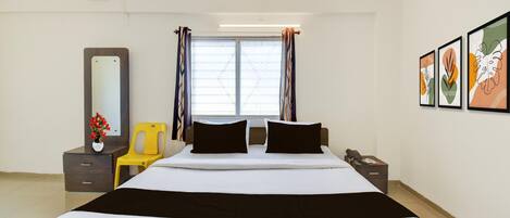 Una habitación de hotel con cama, escritorio, silla, espejo y cuadros en la pared.