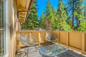 A balcony with two wire mesh chairs and a glass table, overlooking a forested area. - Two-story mountain-view condo with balcony, fireplace & pool - dog-friendly (Incline Village)