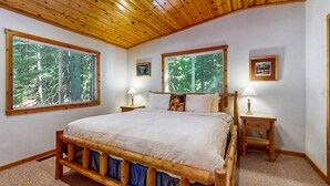 Ein Schlafzimmer mit einem hölzernen Bett, zwei Nachttischen und großen Fenstern mit Blick auf einen Wald.