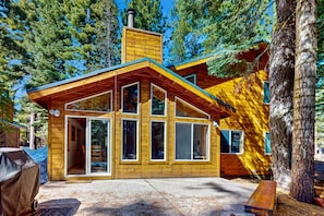 A wooden cabin with large windows, a chimney, and a deck area.