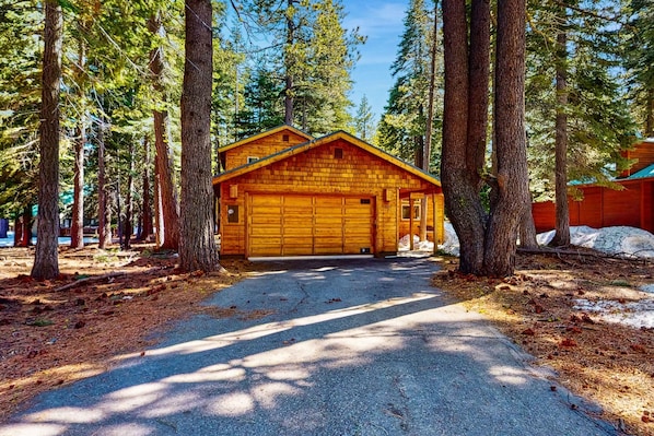 A log cabin with a garage, surrounded by tall trees and a clear sky.