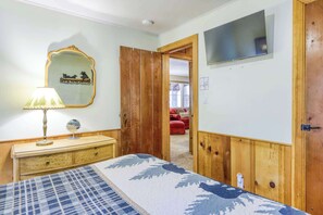 A bedroom with a bed, a dresser, a mirror, a television, and a door leading to another room. - Basecamp on Aspen (South Lake Tahoe)