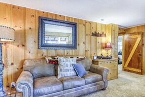 A room with a leather sofa, a wooden wall, a framed mirror, a lamp, and a wooden door. - Basecamp on Aspen (South Lake Tahoe)