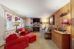 Ein gemütliches Wohnzimmer mit Kamin aus Stein, einem Fernseher und Holzwänden.