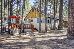A cabin with a wooden deck, a red umbrella, and a staircase leading to the entrance. - Basecamp on Aspen (South Lake Tahoe)