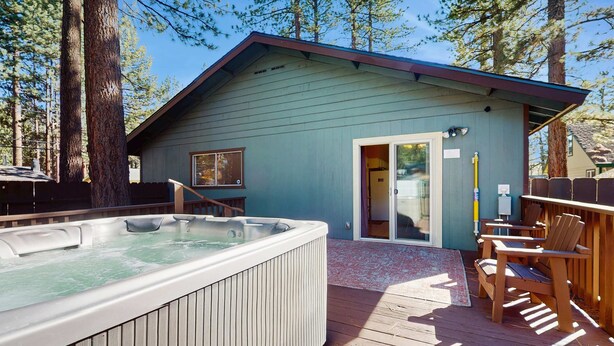 Una terraza de madera con un jacuzzi, sillas de madera y un edificio con puerta corredera de vidrio.
