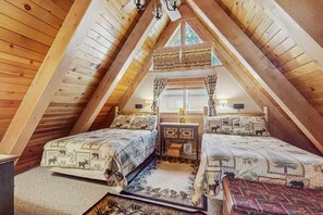 A cozy attic bedroom with two beds, a small table, and a window. - Charming Updated Rustic Cabin with Gas Fireplace, close to Lake and Ski Resort (South Lake Tahoe)
