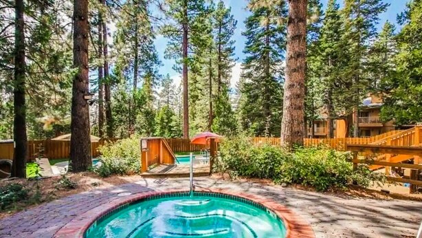 A swimming pool surrounded by a wooden deck, with tall trees in the background. - Cozy Studio with Full Kitchen, Grill, Fireplace w/Access to Pool, Spa, Game Room (Tahoe Vista)