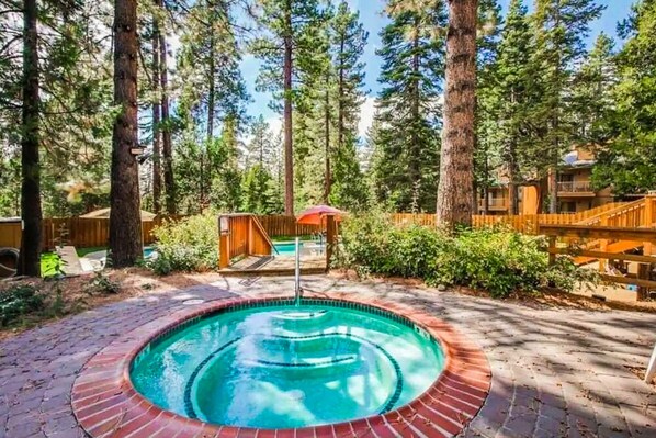 A swimming pool surrounded by a wooden deck, with tall trees in the background. - Cozy Studio with Full Kitchen, Grill, Fireplace w/Access to Pool, Spa, Game Room (Tahoe Vista)