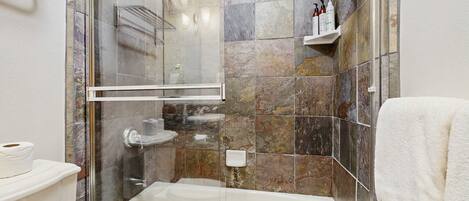 A bathroom with a glass-enclosed shower, a bathtub, a toilet, and a shelf with toiletries.
